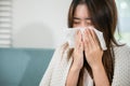 Sick female sitting under blanket on sofa and sneeze with tissue paper in living room Royalty Free Stock Photo