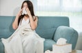 Sick female sitting under blanket on sofa and sneeze with tissue paper in living Royalty Free Stock Photo