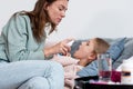 Sick girl lies on the couch and her mother sprays medicine into her mouth