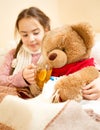 Sick girl lying in bed and giving tea to teddy bear Royalty Free Stock Photo