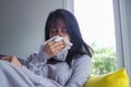Sick girl sitting on the sofa in the house, having a runny nose fever and wiping with a sick handkerchief. cold, sneezing concept Royalty Free Stock Photo