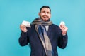 Sick guy wearing dark suit and wrapped in scarf treating flu with pills, looking miserable upset