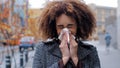 Sick ill african american woman with curly hair blowing runny nose into tissue paper outdoors cold allergies respiratory Royalty Free Stock Photo