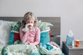 Sick ill Caucasian girl with fever lying in bed at home blowing nose with a napkin paper tissue. Virus cold season flu illness. Royalty Free Stock Photo