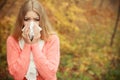 Sick ill woman in autumn park sneezing in tissue.