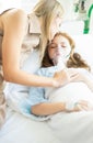 Sick kid girl with oxygen mask laying in bed at hospital and mother`s hand holding together and mom kiss her to support daughter.