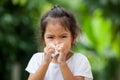 Sick little asian girl wiping or cleaning nose with tissue