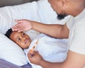 Sick little boy in bed while his father uses a thermometer to check his temperature. Black single parent feeling sons
