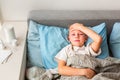 Sick little boy with high fever and headache laying in bed checking his forehead. Stay at home during corona virus epidemic Royalty Free Stock Photo