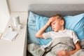 Sick little boy with high fever and headache laying in bed checking his forehead. Stay at home during corona virus epidemic Royalty Free Stock Photo