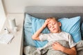 Sick little boy with high fever and headache laying in bed checking his forehead. Stay at home during corona virus epidemic Royalty Free Stock Photo