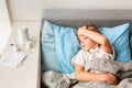 Sick little boy with high fever and headache laying in bed checking his forehead. Stay at home during corona virus epidemic Royalty Free Stock Photo