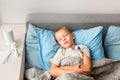 Sick little boy with high fever and headache laying in bed and holding thermometer. Stay at home during corona virus epidemic Royalty Free Stock Photo