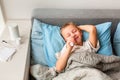 Sick little boy with high fever and headache laying in bed spraying medicine into his nose. Stay at home during corona virus Royalty Free Stock Photo