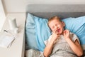 Sick little boy with high fever and headache laying in bed spraying medicine into his nose. Stay at home during corona virus Royalty Free Stock Photo