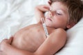 Cute little boy suffering from high temperature fever lying with thermometer in armpit Royalty Free Stock Photo