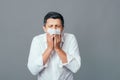 Sick man blowing his nose while standing indoor over gray background. Sneezing Lifestyle Health Medicine People Emotions Pills Royalty Free Stock Photo