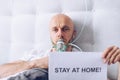 Sick man breathing through oxygen mask and holding card with message stay at home Royalty Free Stock Photo