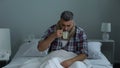 Sick man coughing in bed, drinking antipyretic tea to treat fever, flu epidemic