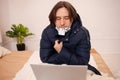 A sick man froze at home. It`s very cold. A man sits in outer clothing behind a laptop wearing a mask. Home quarantine in winter. Royalty Free Stock Photo