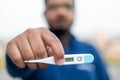 Sick man holds digital thermometer with body temperature reading in Fahrenheit up close to the camera