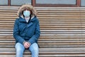 Sick man with hood sitting alone on bench, wearing facial mask. coronavirus pandemic, isolation, quarantine
