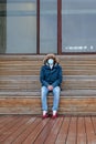 Sick man with a hood sitting alone on bench, wearing protective facial mask. coronavirus pandemic