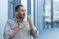 Sick man outside office building has severe sore throat, businessman outside office building uses aerosol medicine for