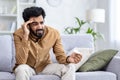 Sick man sitting at home on sofa in living room, sneezing has allergy and runny nose, Indian man with napkin has a cold Royalty Free Stock Photo