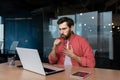 Sick man at workplace, mature worker in red shirt coughing, businessman inside office at work using laptop Royalty Free Stock Photo