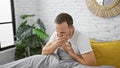 Sick middle age man with grey hair sitting in bed, coughing his lungs out in the solitude of his bedroom, battling the flu in the Royalty Free Stock Photo