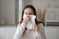 Sick millennial woman having cold blowing nose in paper tissue