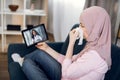 Sick Muslim woman patient suffering from cold, covid and running nose, sitting on sofa at home, talking with her doctor
