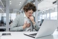 Sick office worker, young male businessman sits at the desk with a laptop and documents and coughs, covers his mouth Royalty Free Stock Photo