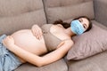 Sick pregnant woman is lying on the couch at home. Protect your health with protective medical mask. infection. Global