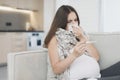 Sick pregnant woman sitting at home on the couch. It measures temperature with an electronic thermometer Royalty Free Stock Photo