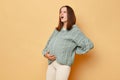 Sick pregnant woman wearing knitted warm sweater standing isolated over beige background touching her painful back bad feeling Royalty Free Stock Photo