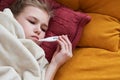 Sick preteen girl laying in bed using thermometer