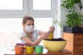 A sick quarantined girl pours earth into a pot for planting plants