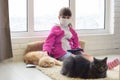A sick quarantined girl sits on the floor with a tablet, cats are lying next to the carpet