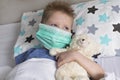 A sick sad child in a mask with a temperature and a headache lies in bed. Flu colds disease virus