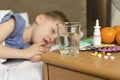 A sick sad child with a temperature and a headache lies in bed next to medicines and pills. Flu colds disease virus