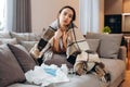 Sick sad girl sitting on the sofa covered with a blanket. There are many used napkins in the background Royalty Free Stock Photo