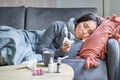 Sick sad korean woman lying on sofa, feeling unwell, catching cold, flu and temperature, looking upset, taking Royalty Free Stock Photo