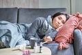 Sick sad korean woman lying on sofa, feeling unwell, catching cold, flu and temperature, looking upset, taking Royalty Free Stock Photo