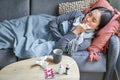 Sick sad korean woman lying on sofa, feeling unwell, catching cold, flu and temperature, looking upset, taking Royalty Free Stock Photo