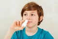 Sick school boy with runny nose using nasal medicine spray. Boy has a virus, runny nose and headache Royalty Free Stock Photo