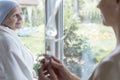 Sick senior looking at a nurse putting on a drip-bag in a hospital. Blurred photo