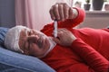 A sick male checking thermometer lying with wet towel on his forehead Royalty Free Stock Photo