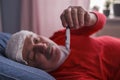 A sick male checking thermometer lying with wet towel on his forehead Royalty Free Stock Photo